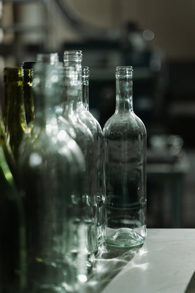 Row of clear glass bottles in a dimly lit industrial environment, highlighting texture and design.